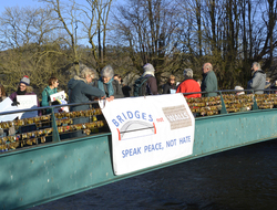 Quakers in Bakewell on a bridge with a banner saying 'bridges not walls'