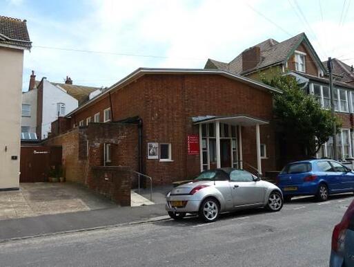 Large brick building with column-flanked entrance and red sign reading 'Quaker Meeting House'.