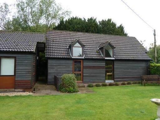 Grey wooden building with dormer windows, set within garden grounds.