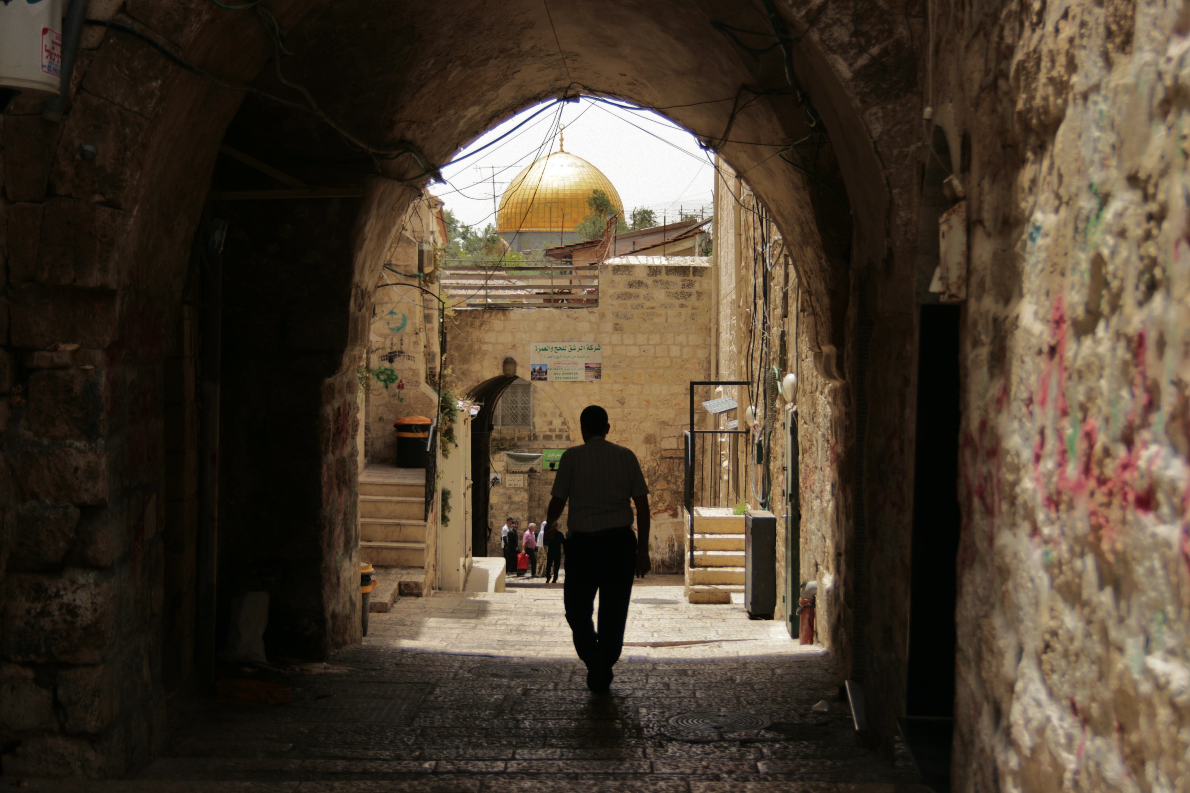 A person in shadow walking through into the light with the golden dome of a mosque shining in the sunlight