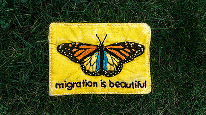 Homemade embroidered butterfly on a bright yellow background with words 'migration is beautiful'