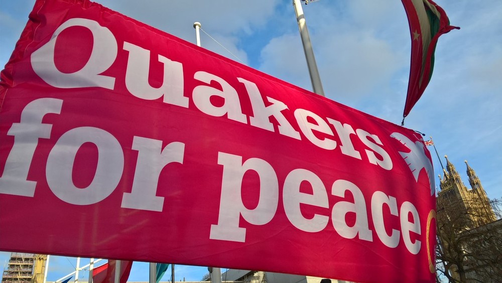 Bright pink Quakers for Peace banner against a blue sky