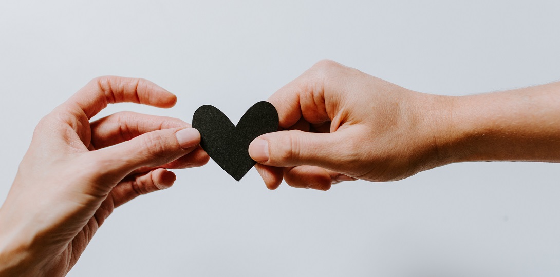 A photograph of two hands holding a black cut-out heart