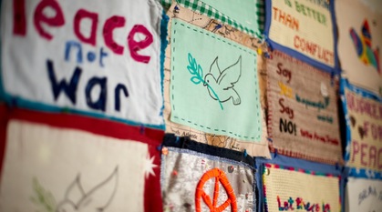 A peace dove appliquéd onto a textile panel with other peace messages on textile panels blurred around it