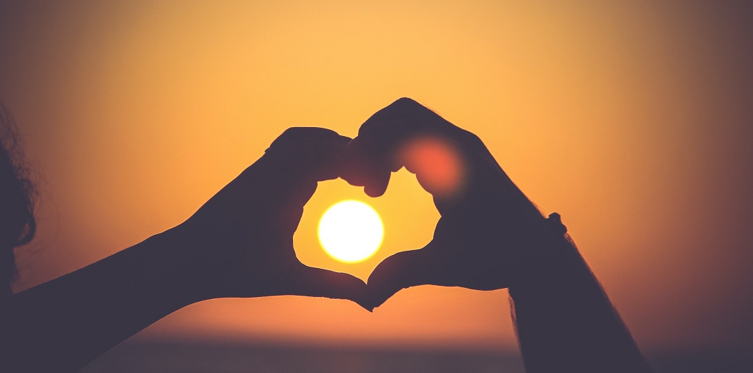 Hands making a heart shape around a setting sun.