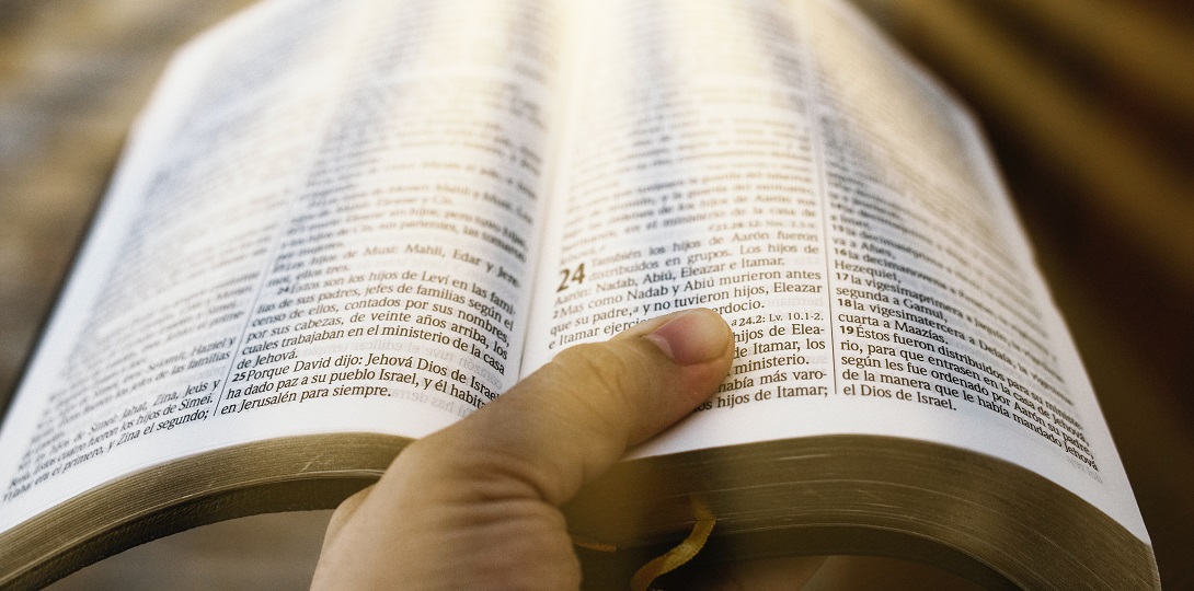 A male hand holding an open Bible with light shining on it.