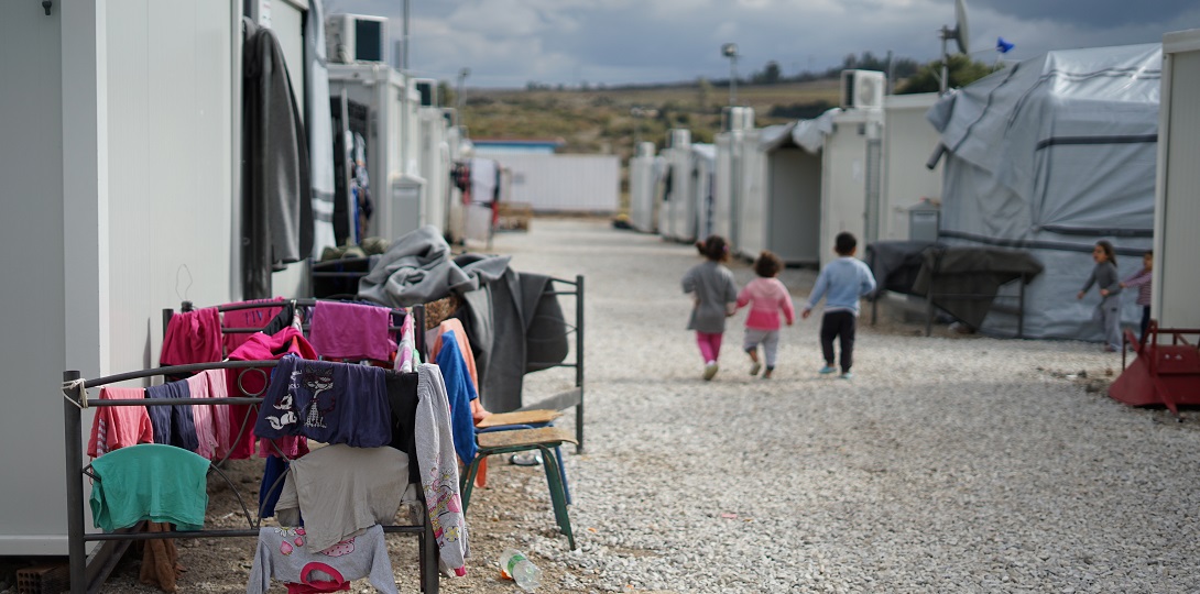 An image of a refugee camp with three young children walking away from the camera