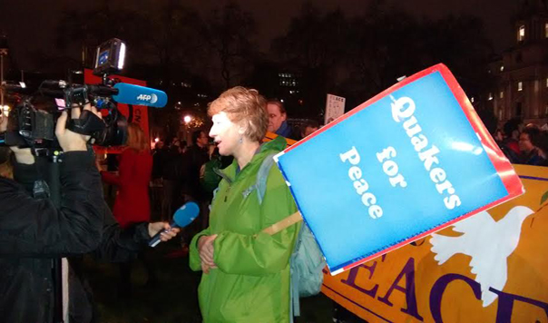 Woman with "Quakers for Peace" placard talks to television crew