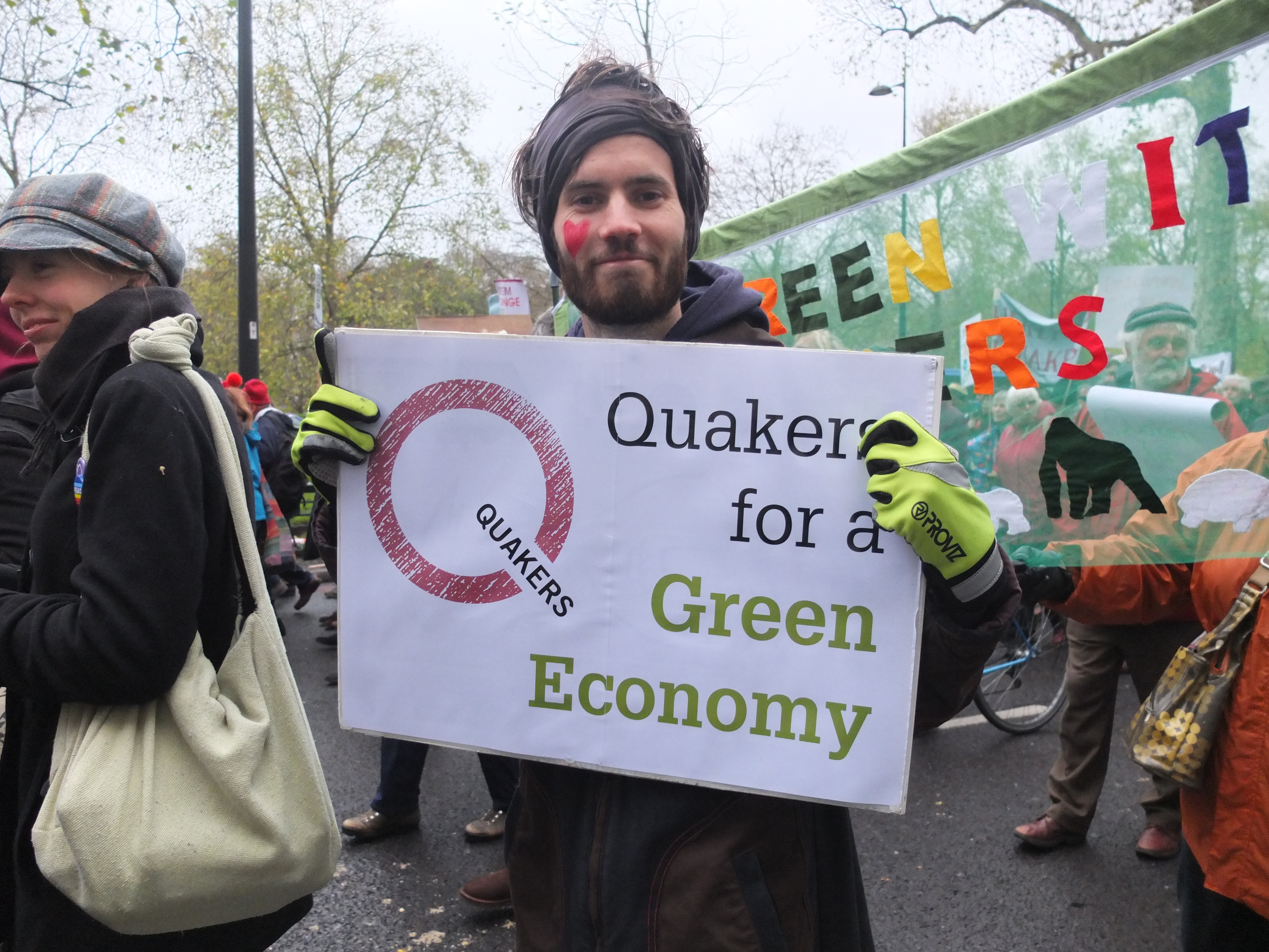 young man with facepaint holds a banner saying Quakers for a green economy