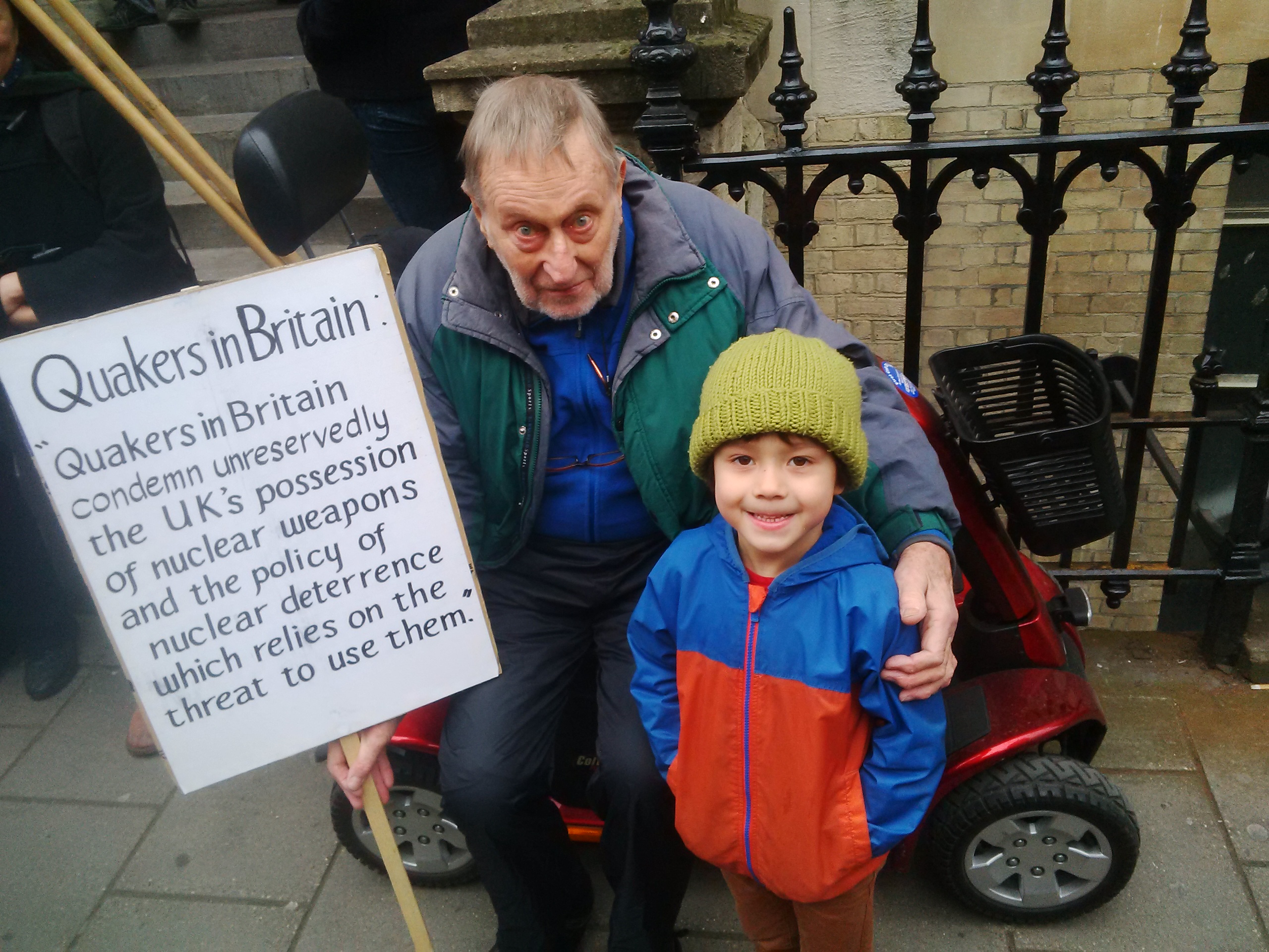 Man and boy holding a poster saying "Quakers in Britain condemn unreservedly the UK's possession of nuclear weapons and the policy of nuclear deterrence which relies on the threat to use them"
