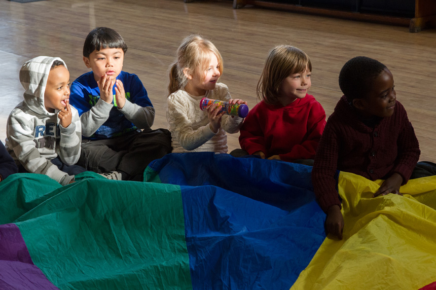 Five young children play with brightly coloured parachute and rainsticks