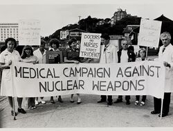 A group of doctors and nurses hold up a "Medical Campaign Against Nuclear Weapons" banner and placards