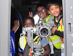 Several small boys grin as they crowd behind a machine gun pointing out of an aircraft