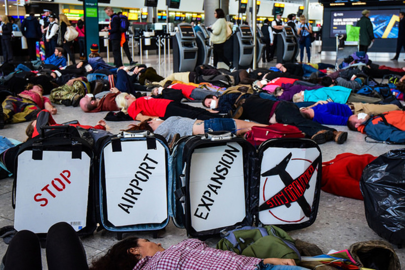 people lying on the ground pretending to be dead. Sign reads stop airport expansion stay grounded. 