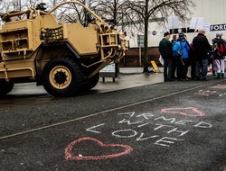 Protesters stand outside the arms expo in Hereford next to their words "Armed with Love" chalked on the floor