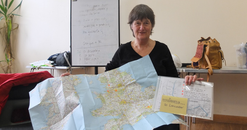 A woman holding up a map of the UK and Ireland and a pack entitled 'Welcome to Lancaster'