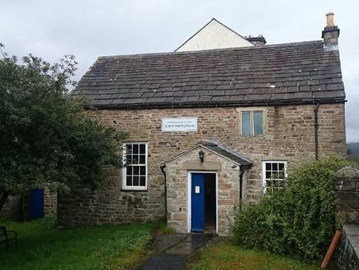 Small stone building with blue front door in a large garden.