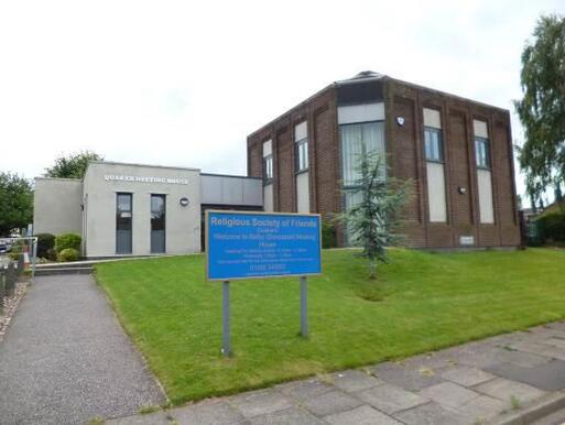 Large red brick building with grey stone extension and blue sign 'Religious Society of Friends'.