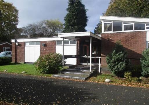 One storey brick building with a flat roof which extends out over the front entryway to shelter 3 steps. 