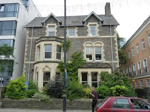 Converted three storey grey stone townhouse with decorative detailing surrounding the large two-level bay windows. 