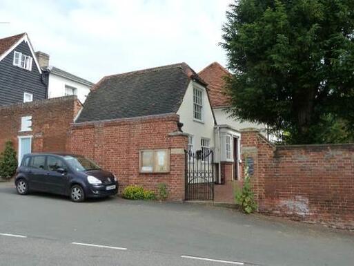 White detached house separated from the road by a gate leading to a garden and burial area. 