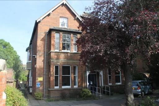 Three storey brick semi-detached house, its front door and entry slope are shaded by large trees. 