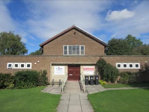 Two storey brick building with large red front doors. The building is accessed by a slope which runs through a large lawn. 