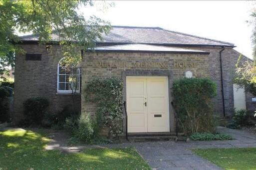 Grey stone building with large white entrance doors set within a garden. 