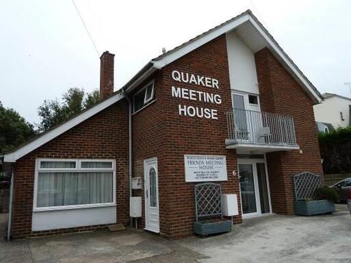 Large brick house with high roof peak and large white lettering reading 'Quaker Meeting House'.