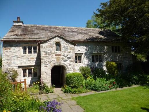 Large stone house with arched entryway and wide cottage gardens. 