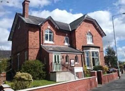 Large redbrick house with pointed feature windows and steps leading to the pale green front door. 