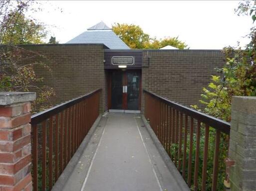 Low brick building connected to the street by a bridge leading to entrance doors. 