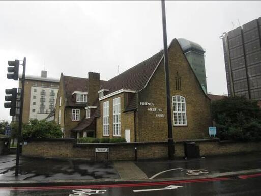 Brick building with long dual level windows and 'Friends Meeting House' lettering, building is situated on a busy road next to a cycle path. 