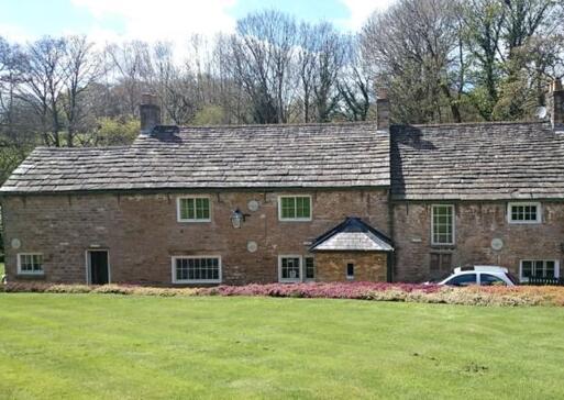 Long stone cottages are partially obscured behind a raised large lawn and flowerbeds. 