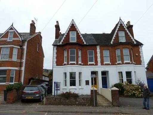 Semi-detached red-brick house with decorative white brickwork, yellow front door, and slope to entrance.