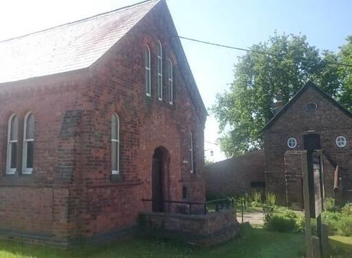 Old redbrick chapel with high roof peak within large garden grounds.