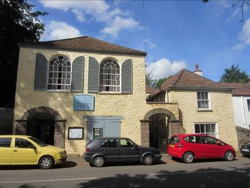 Sand coloured building with large arched windows surrounded by grey shutters. 