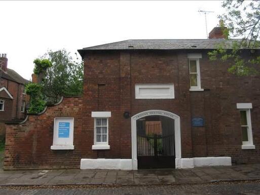 Brick house with white painted archway which has 'Friends Meeting House' black lettering. 