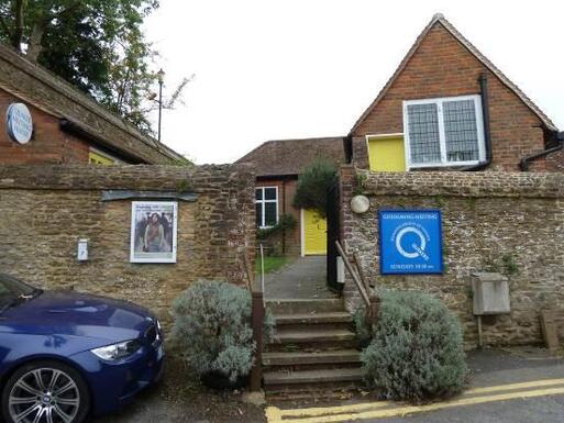 Stone cottage with yellow doors flanked by high stone walls, a large blue Q Quaker sign is attached to the right boundary wall.
