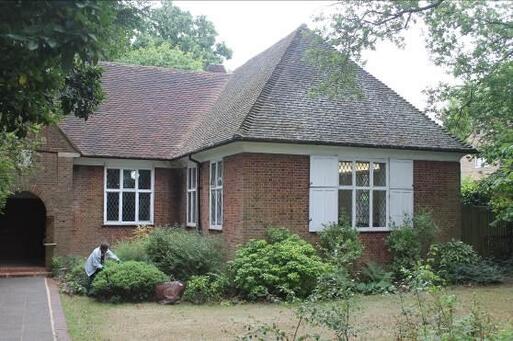 Brick bungalow with white shuttered windows is within pleasant gardens.