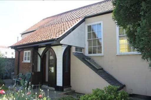 White building with large sloping entrance porch, all framed with black wooden detailing.