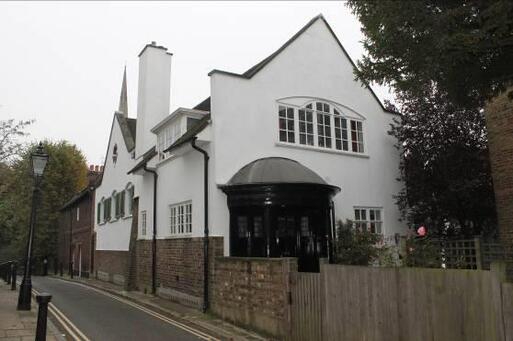 Large white house with rounded black entrance porch separated from the street by a small garden fence.