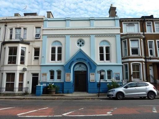 Light blue terraced building with white decorative elements and a large dark blue entrance arch with 'Friends Meeting House' lettering.
