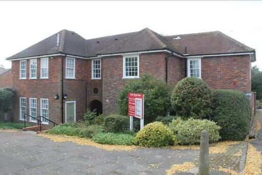 Large brick house with large windows and bright red noticeboard in its small front garden.