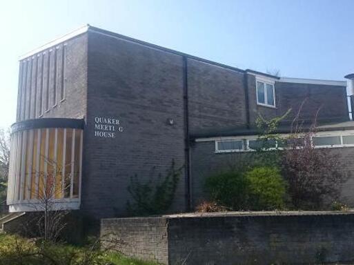 Two-storey modernist grey brick building with large feature bay window and Quaker Meeting House white lettering. 