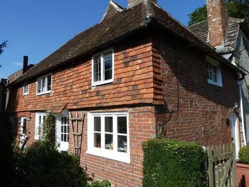 Two storey brick cottage with a low roof and decorative period features.