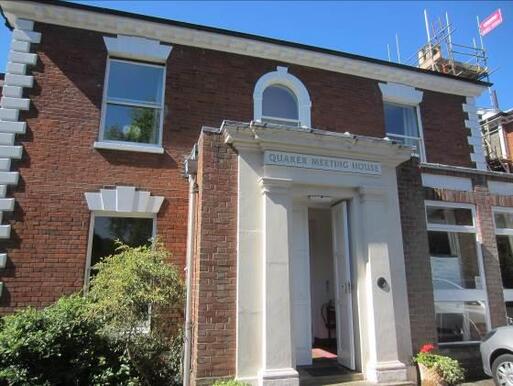 Red brick classical villa with a simple doorway surrounded by stone pillars reading Quaker Meeting House.
