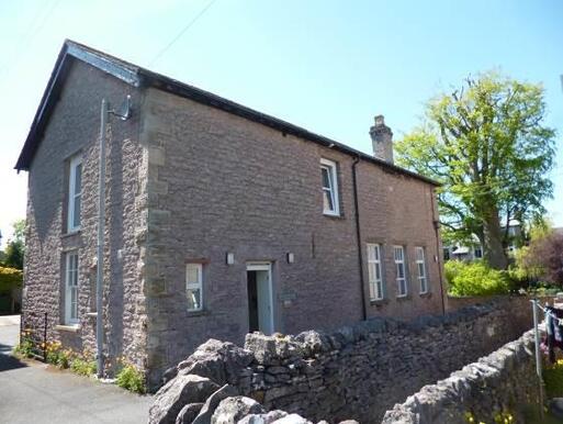 Former stable building is surrounded by stone boundary wall and garden grounds.