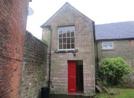 Small stone building with single large window and red front doors.
