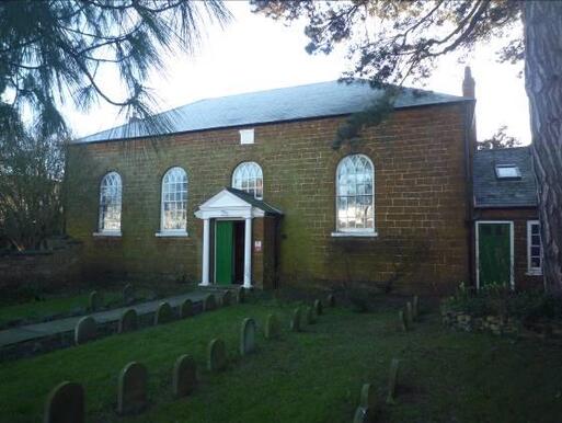 A plain but handsome ironstone building with four main windows and green doors.